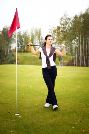 Young woman golf player posing on green with club, ball and cupの写真素材