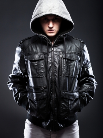 Young man in leather jacket with a hood on darkness backgroundの写真素材