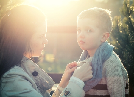 Mother dressing child in scarf while walking outdoorの写真素材