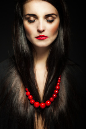 Beautiful glamour woman with dark shiny hair, long eyelashes and red beadsの写真素材