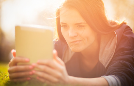 Beautiful girl using tablet or ebook outdoor laying on fieldの写真素材