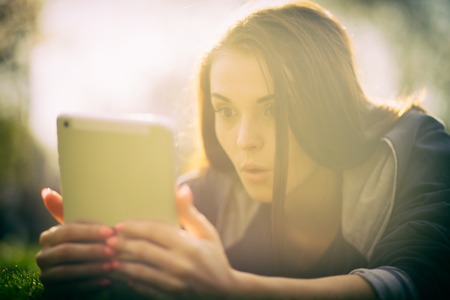 Beautiful girl using tablet or ebook outdoor laying on fieldの写真素材