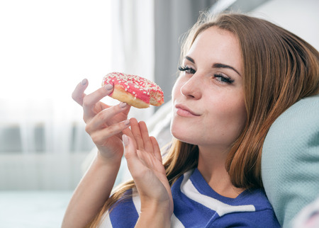 Woman at home eating fresh red donut and relaxingの写真素材