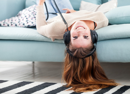 Young woman with headphones lying on sofa and listening to music at homeの写真素材
