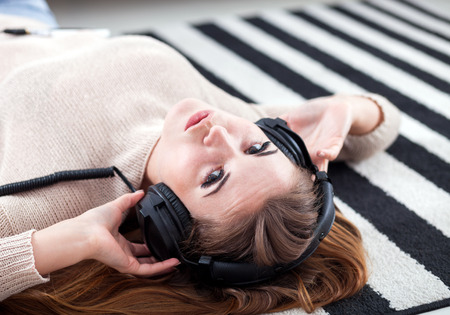 Young woman with headphones lying on floor and listening to music at homeの写真素材