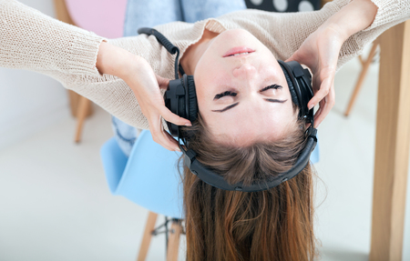 Young woman with headphones sitting on chair and listening to music at homeの写真素材