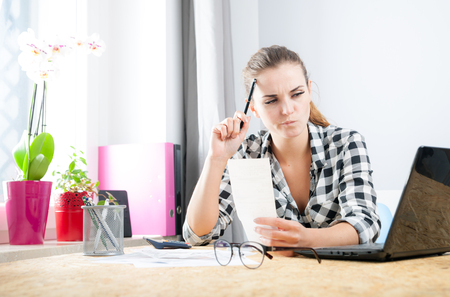 Young woman calculating and paying bills in home officeの写真素材