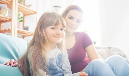 Mother and daughter sitting on sofa at home, happy loving familyの写真素材