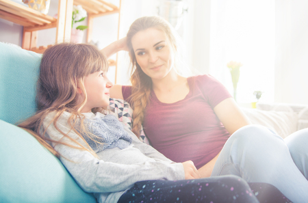 Mother and daughter sitting on sofa at home, happy loving familyの写真素材