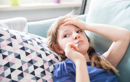 Sick little girl lying in bed at home with thermometerの写真素材