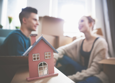 Young couple with small wooden house at their new home among cardboard boxesの写真素材