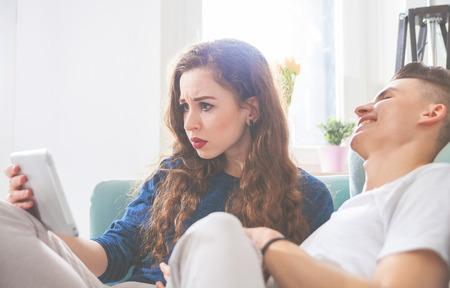 Young couple on sofa at home using digital tabletの写真素材