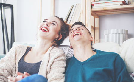 Young loving couple on sofa at home laughing togerherの写真素材
