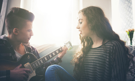Young couple playing the guitar and singing on sofa at homeの写真素材