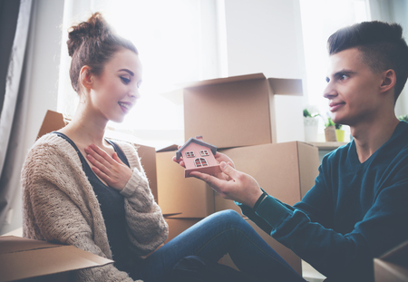 Young couple with small wooden house at their new home among cardboard boxesの写真素材