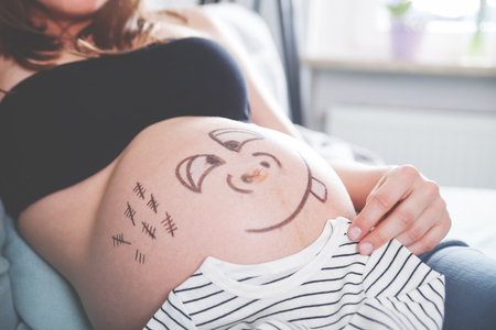 Close up of pregnant belly with happy smiley faceの写真素材