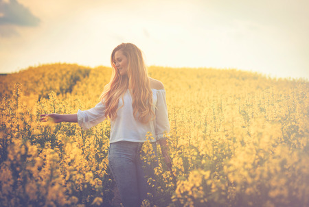 Happy smiling woman in yellow rapeseed field at sunsetの写真素材