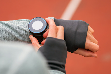 Athletic woman on running track setting up her smart watch, fitness accessoriesの写真素材