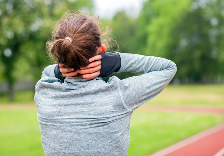 Athletic woman on running track touching hurt neck with painful injury during workoutの写真素材