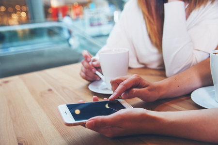 Two friends woman in cafe using mobile phone and texting, close upの写真素材