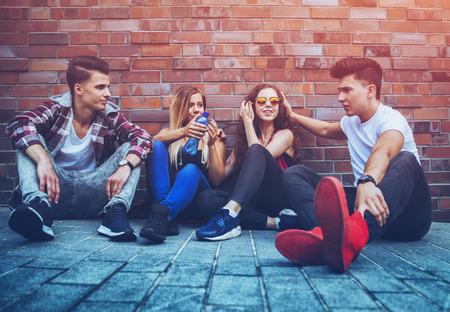 Group of young friends sitting together on street and talkingの写真素材
