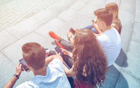 Group of friends sitting together using their mobile phonesの写真素材
