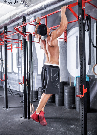 Bodybuilder showing muscular back during pull up exercise at gym