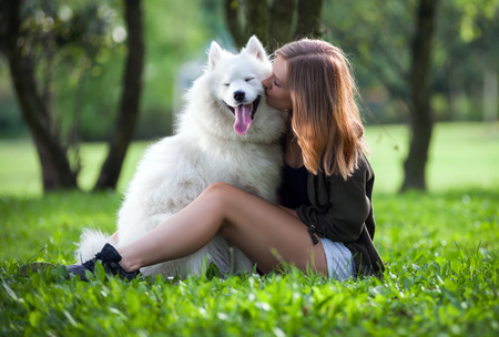 Pretty girl hugging and kissing her dog at the park outdoor, samoyedの写真素材