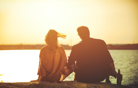Happy couple sitting at the beach during sunset, love and friendship concept