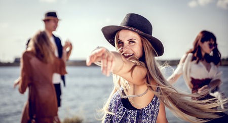 Beautiful styled hippie girl dancing at the beach with group of friendsの写真素材