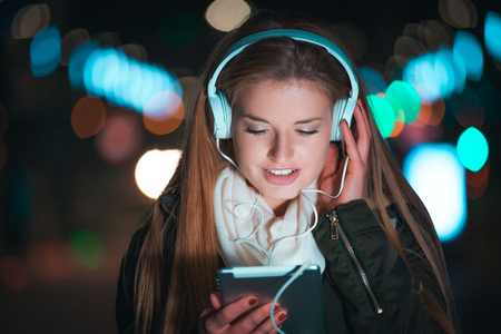 Woman with headphones using tablet and listening music in the city at nightの写真素材