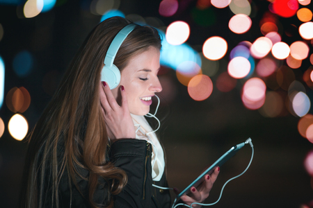 Woman with headphones using tablet and listening music in the city at nightの写真素材
