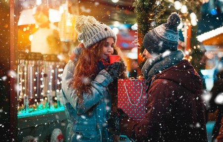 Christmas market restaurant at evening with snowfall, young couple with hot drinks in fairy surroundingsの写真素材