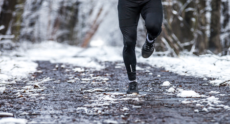 Legs of runner on snowy dirt, warm sporty clothes for winter trainingの写真素材