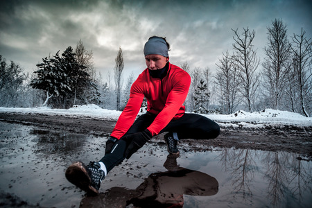 Stretching before running in dirty puddle at winter time, outdoor exercise