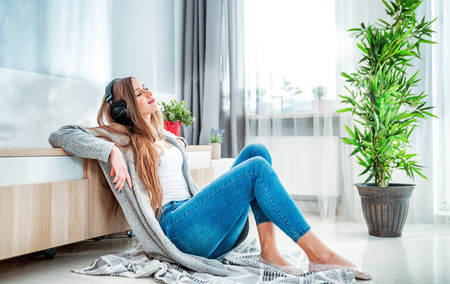 Young woman with headphones listening to music at home in living roomの写真素材