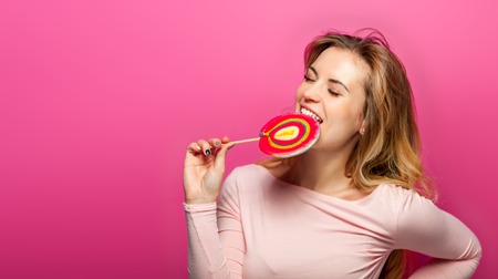 Beautiful young woman with big lollipop over pink backgroundの写真素材
