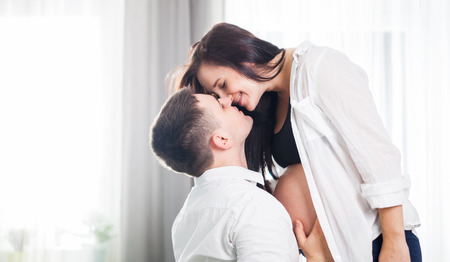 Pregnant couple hugging and kissing at home, expecting babyの写真素材