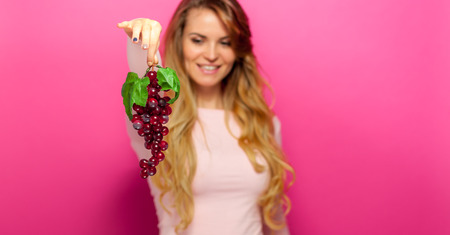 Woman with grape over pink backgroundの写真素材