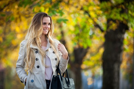 Cheerful young woman walking in the city under colorful autumn treesの写真素材