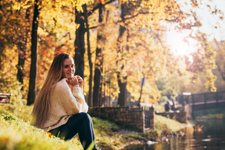 Relaxed woman by lake in the colorful autumn park, carefree timeの写真素材