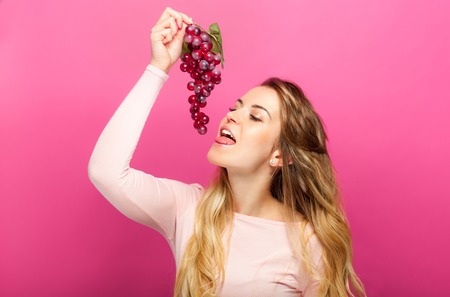Funny woman eating grapes over pink backgroundの写真素材