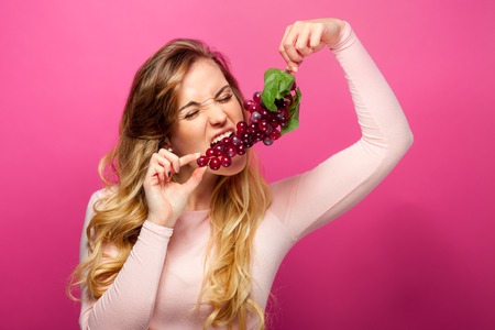 Funny woman eating grapes over pink backgroundの写真素材