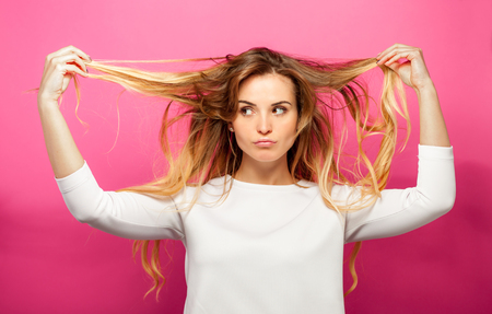 Beautiful blonde woman over pink background has problem with her long hairの写真素材