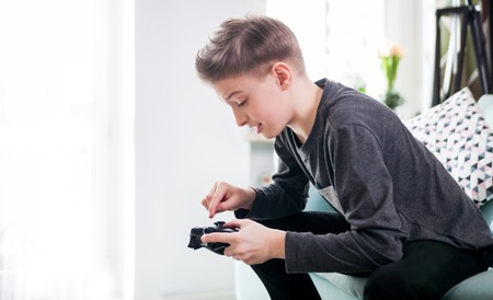 Excited young boy playing game on the console sitting on coach at home