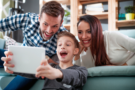 Happy family on sofa at home taking selfie photo using digital tabletの写真素材