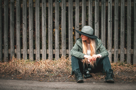 Stylish woman with vintage camera sitting on road at rural countryの写真素材