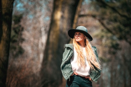 Portrait of beautiful woman with long blond hair in hat walking in forest at sunny day