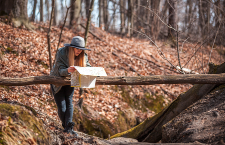 Traveler woman in hat with map in autumn forest, trekking tourism conceptの写真素材