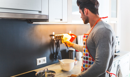 Handsome young man preparing food in the kitchen at homeの写真素材